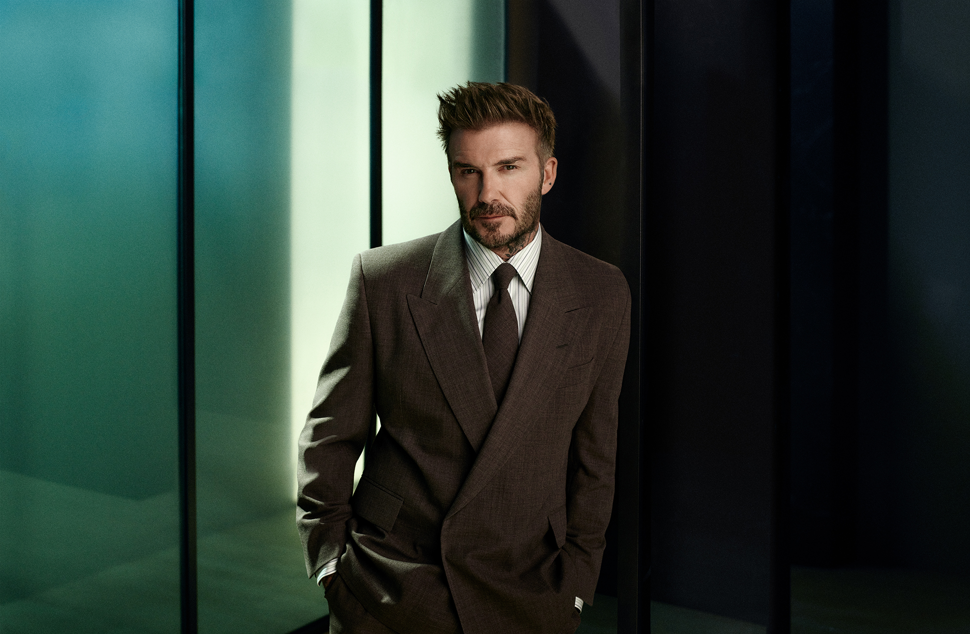 David Beckham in einem stilvollen braunen Hugo Boss Anzug, posiert vor einem modernen, minimalistischen Hintergrund als Teil einer Herrenmode-Werbekampagne.